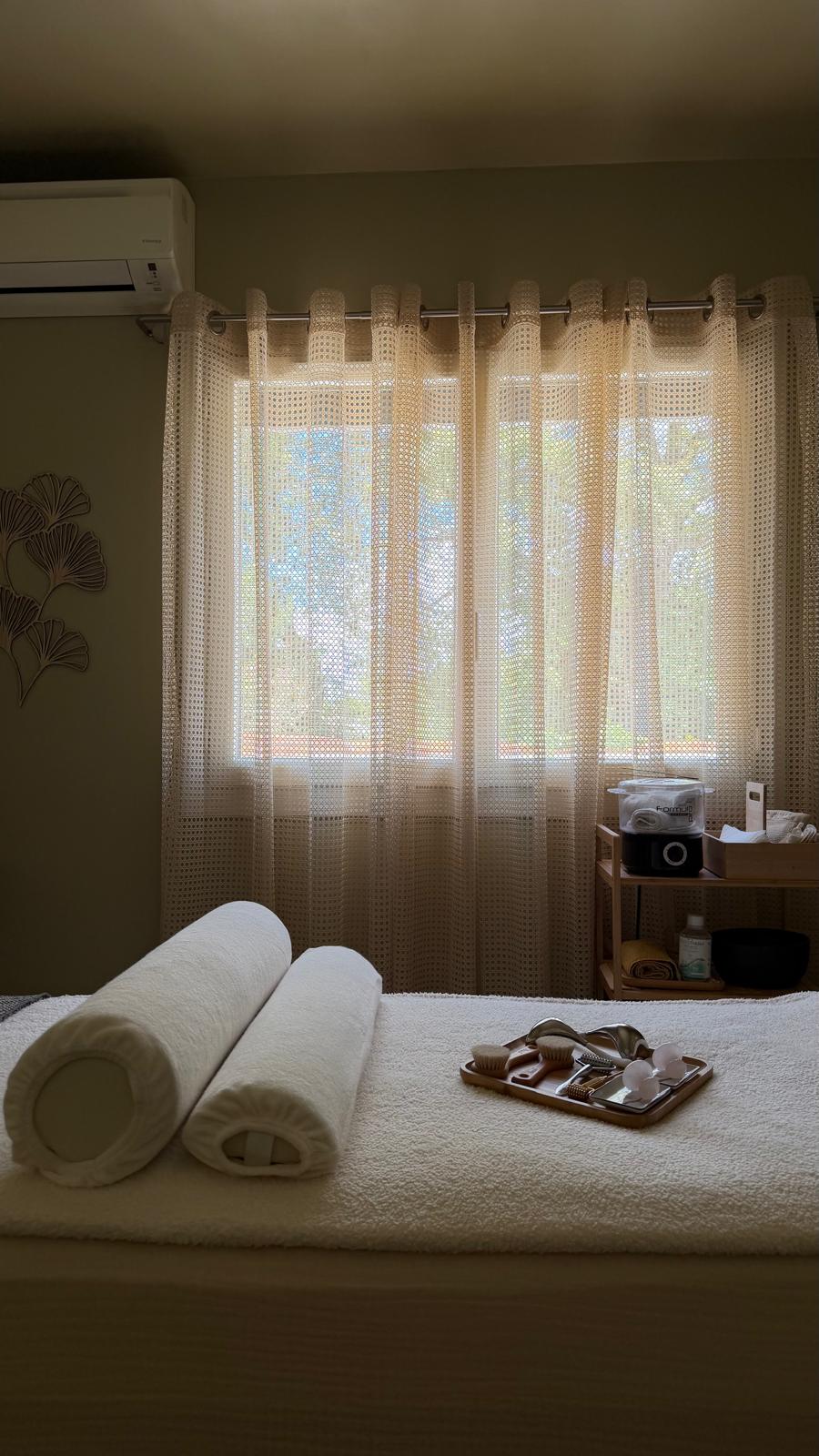 Serviettes roulées sur la table de massage, à contre-jour de la fenêtre.